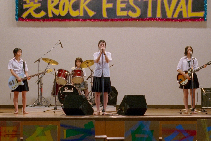 All-girl rock band performing at a festival, wearing school uniforms.