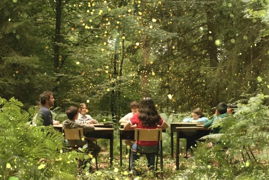 An adult and children seated at a table in a forest.