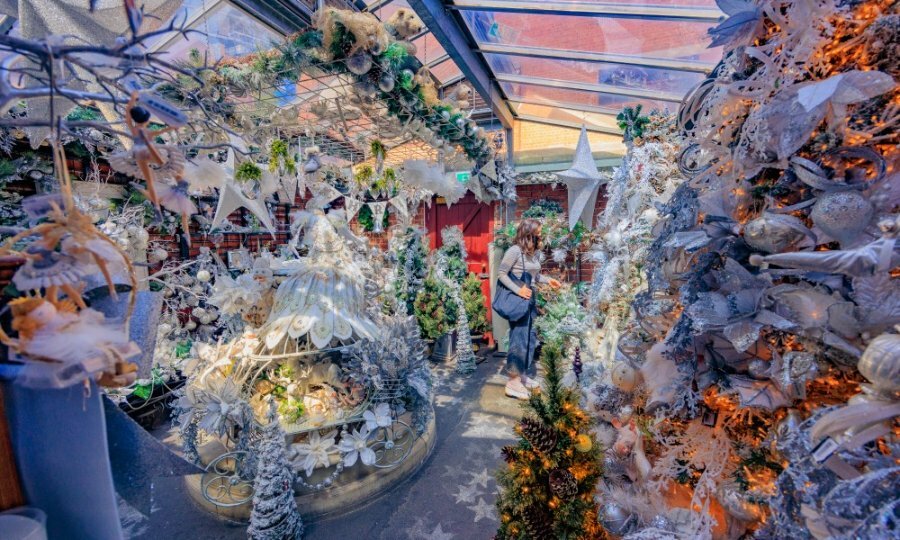 A woman walking through a Christmas shop filled with white decorations.