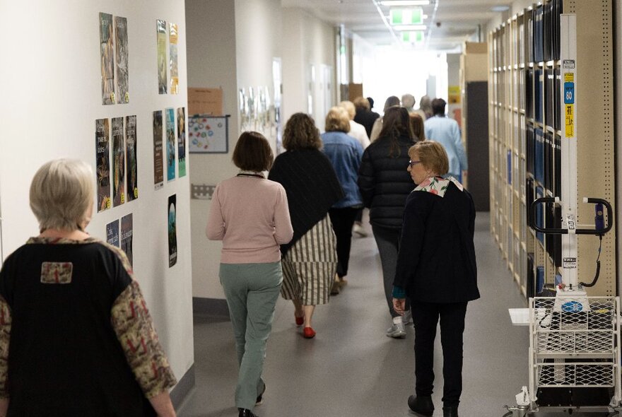 A group of people on a behind-the-scenes tour of the Melbourne Museum, walking through a corridor with pigeon hole shelving on the wall.