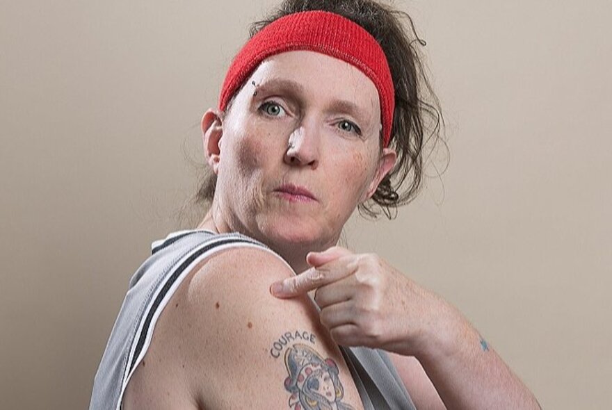 Older woman with tattooed arms, pointing at her shoulder.