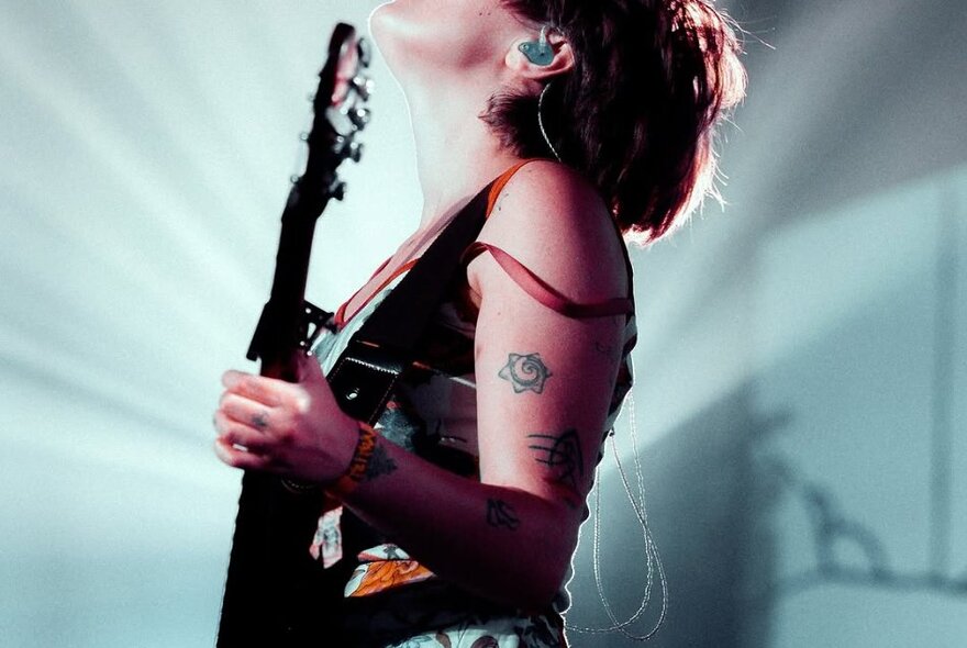 Side view of a torso of a woman holding a guitar and looking upwards. 