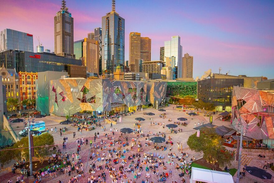 People milling around Fed Square at sunset.