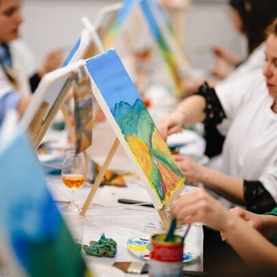 Workshop participants painting on small canvases, at a long workshop table.