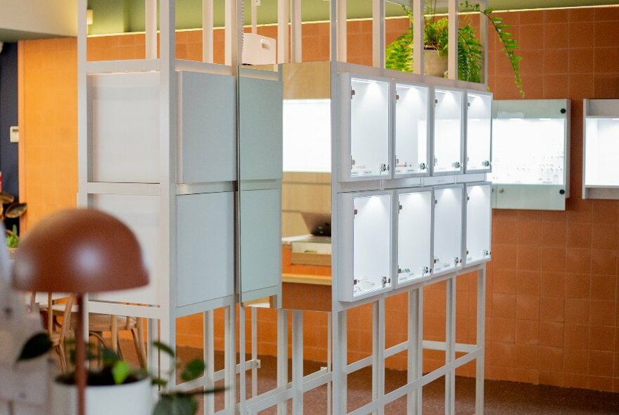 Interior of egetal shop with illuminated display cases, lamps and hanging plants.