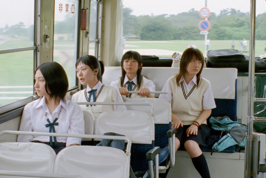 Four girls in school uniform seated at the back of a bus.