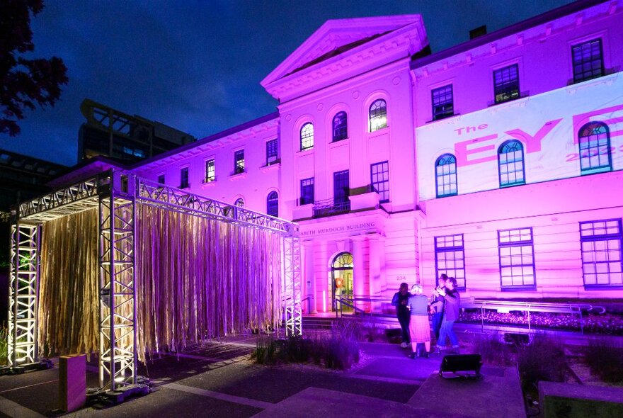 A college building illuminated with a pink / purple light at night. 