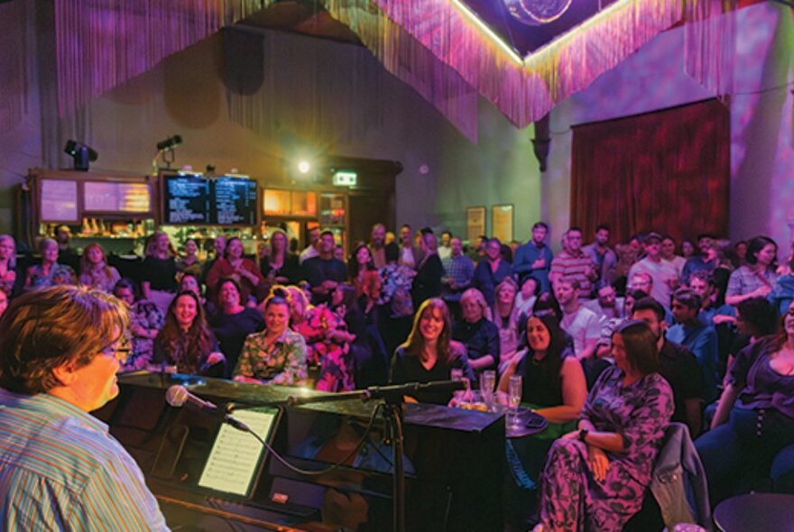 A large performance room with an audience watching a pianist. 