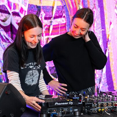 Two smiling DJs standing in front of a DJ deck.