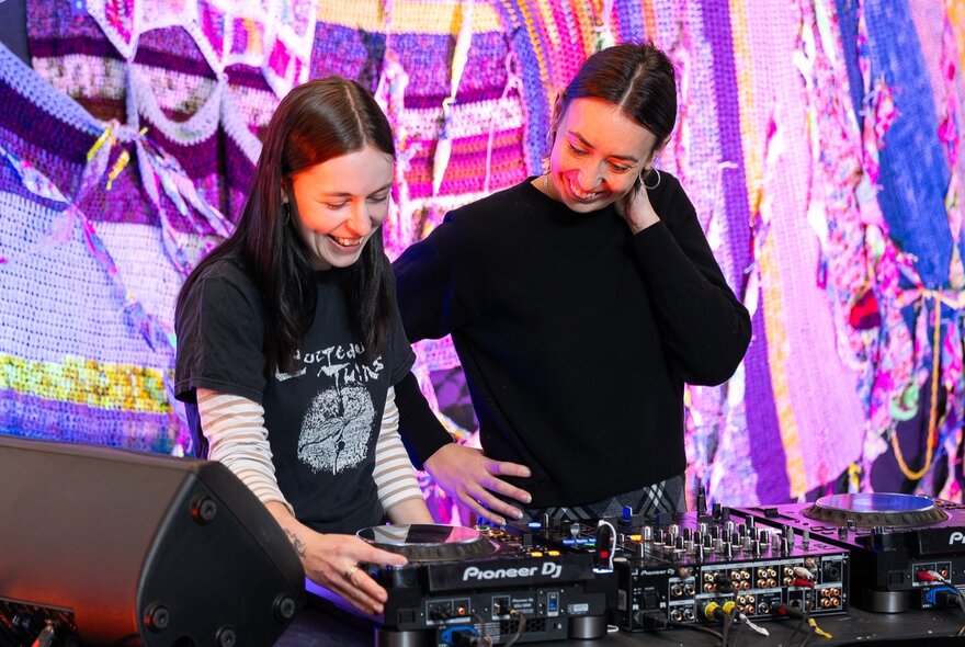 Two smiling DJs standing in front of a DJ deck.