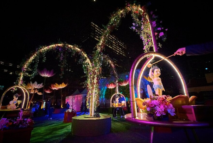 Illuminated display with floral arches and statues on podiums.