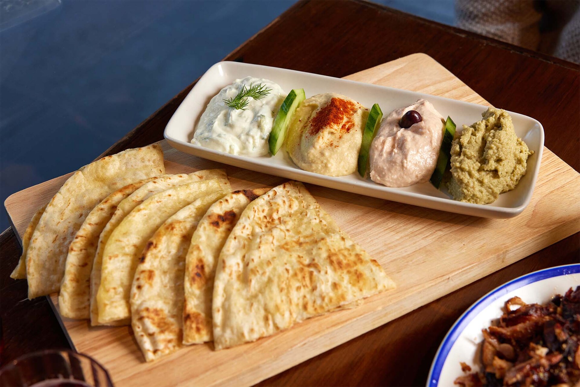 A wooden platter with flat breads and dips on it
