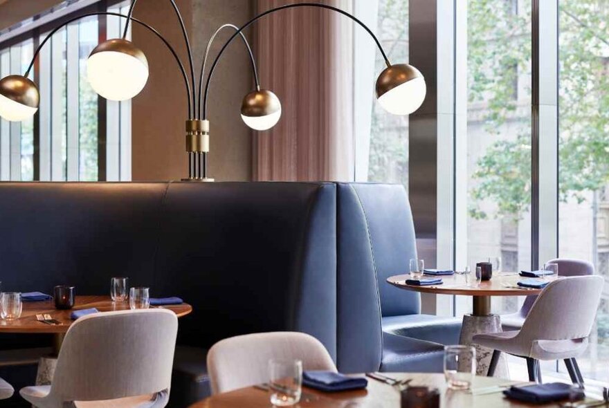 Interior of a restaurant showing tables, deep blue banquettes and lights on curved stems.