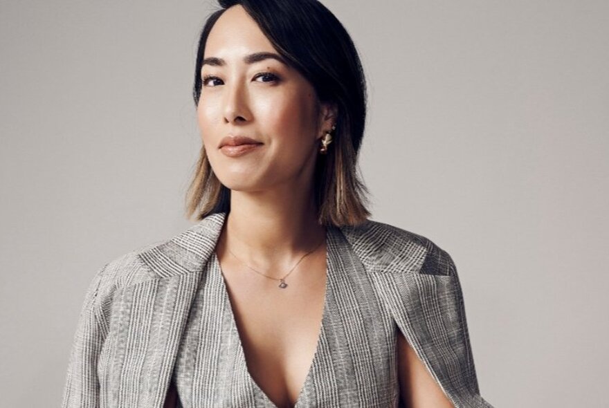TV presenter and writer Melissa Leong with a cheeky side-smile wearing a checked jacket over a matching waistcoat and not shirt. 