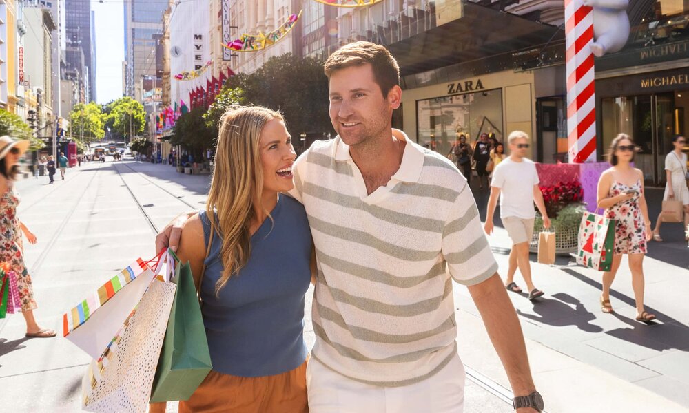 A man and woman holding shopping bags as they walk along Bourke Street Mall. 