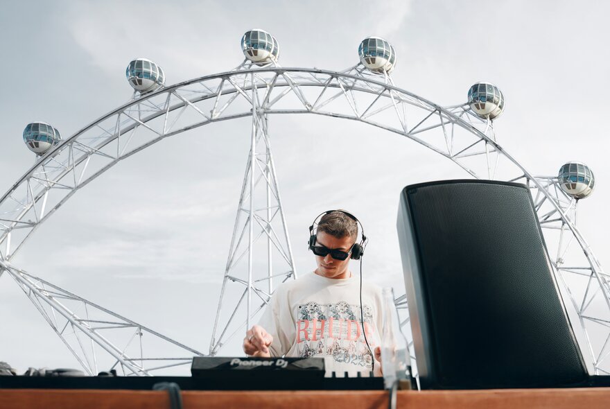 A DJ on the decks with headphones on in front of the Melbourne Star. 