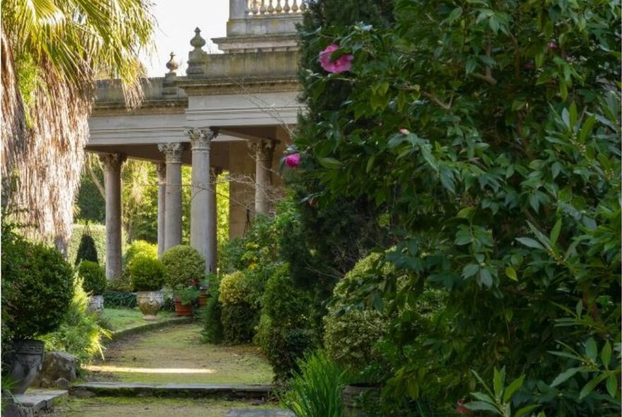 Grand porch and portico of an Italianate villa behind lush gardens.