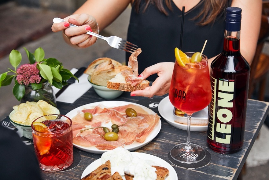 Woman eating from plate of food with cocktails on table. 