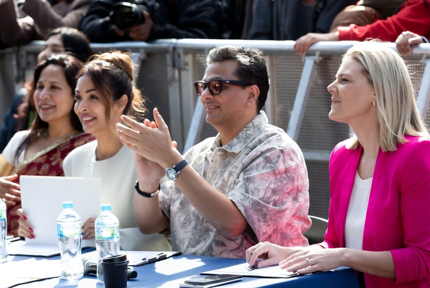 A panel of judges seated at desk smiling, one man clapping.
