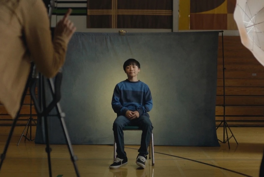 A still shot from the film, Dìdi, with an adolescent Taiwanese American boy sitting on a chair having his school photo taken.