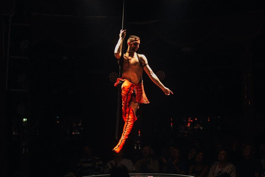 A burlesque performer hanging from a pole on stage.