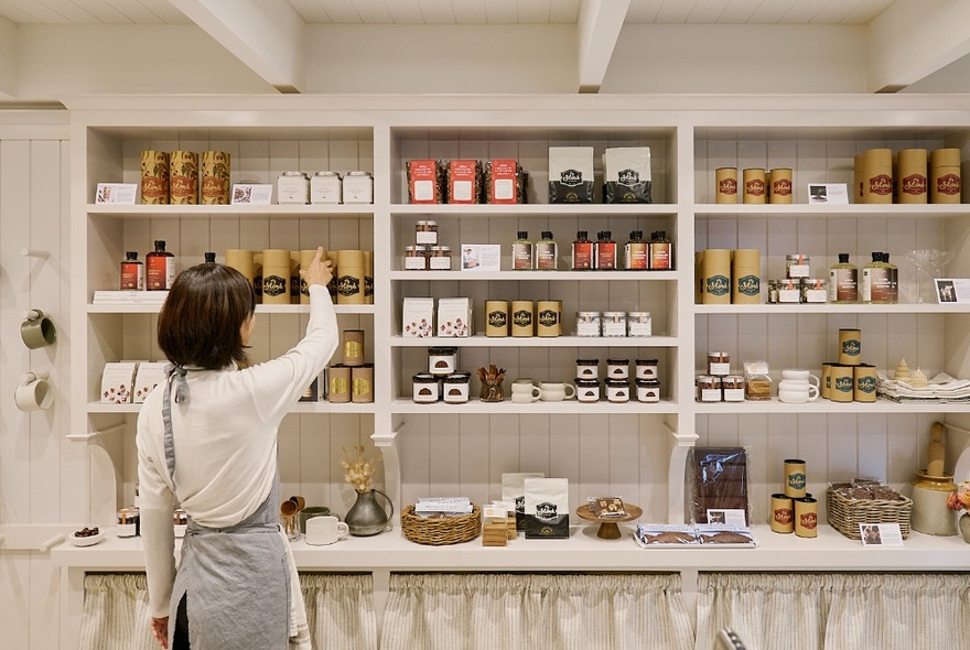 A person neatly arranging products on the white shelves of a Mork Chocolates retail shop.