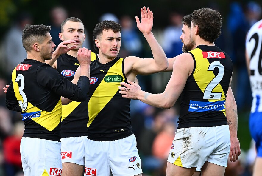 A group of Richmond AFL football players high-fiving and celebrating in a huddle on the field.