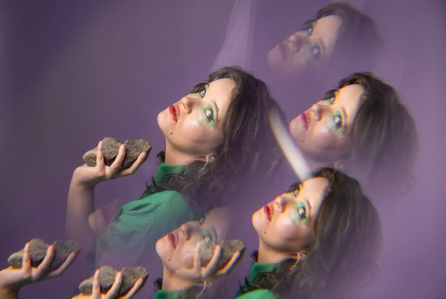 Comedian wearing green eye makeup and shirt, holding rocks in her hands.