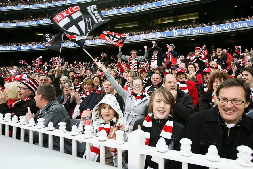 St Kilda AFL fans waving flags and banners in the stands during a match.