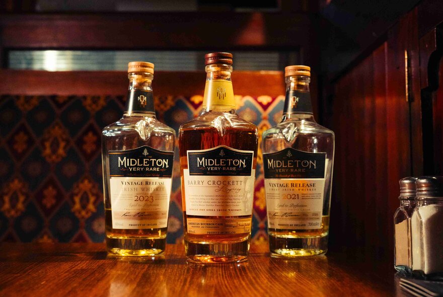 Three bottles of Midleton Irish Whiskey on a wooden bar counter.