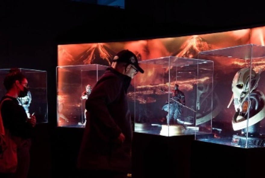 People looking at glass cases of Star Wars memorabilia at an exhibition. 