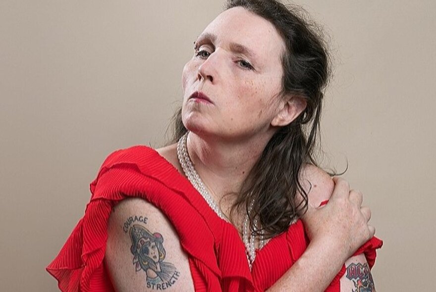 Older woman with tattooed arms, a tough expression on her face.