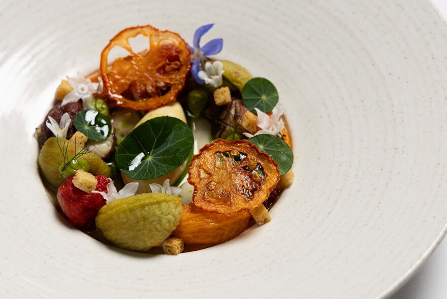A large white bowl with a small circle of vegetables and herbs in the centre.