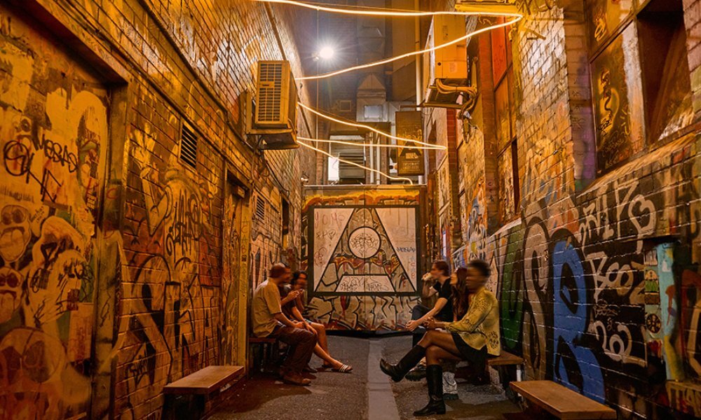 A group of friends sitting on benches in a graffiti covered laneway