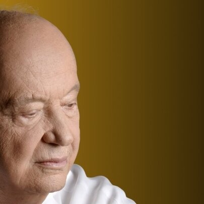 Side view of the head of Greek composer Mimis Plessas, a bald man wearing a white shirt with his eyes looking downwards.