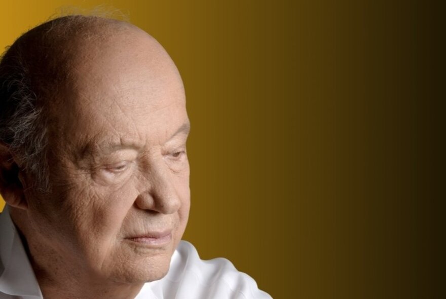 Side view of the head of Greek composer Mimis Plessas, a bald man wearing a white shirt with his eyes looking downwards.