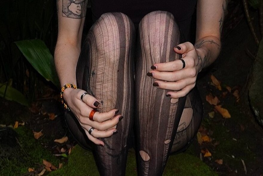Hands holding legs in laddered black tights.