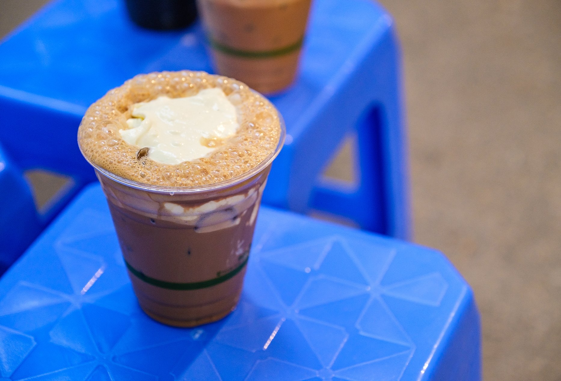 An iced coffee with foam and cream on top on a blue plastic stool.