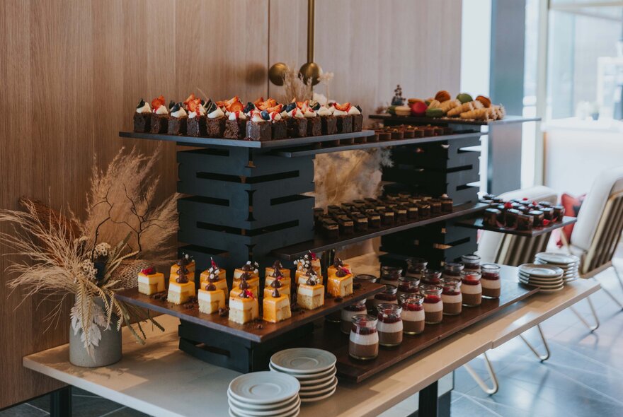 A dessert buffet station set up for an afternoon tea, with small plates and mini desserts arranged on large trays.
