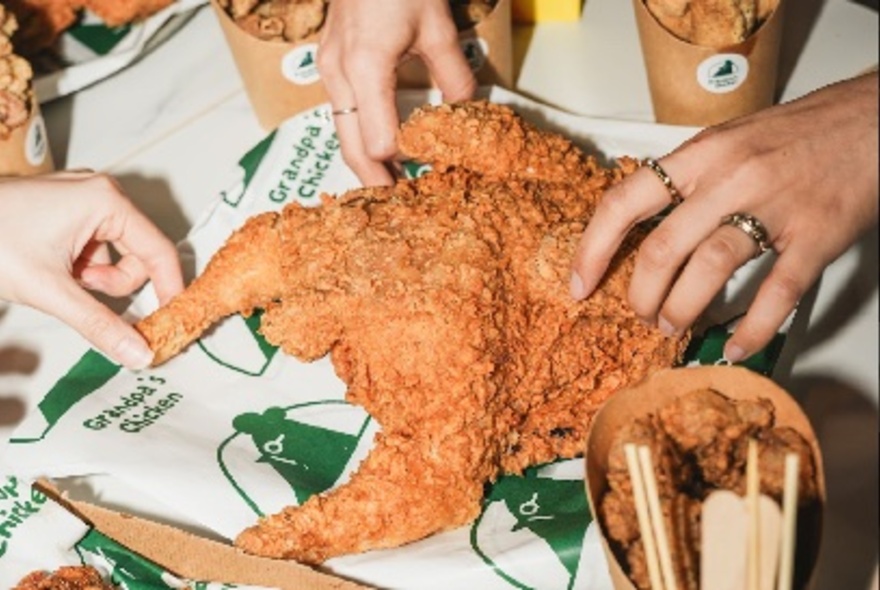 Hands breaking apart an entire fried chicken.