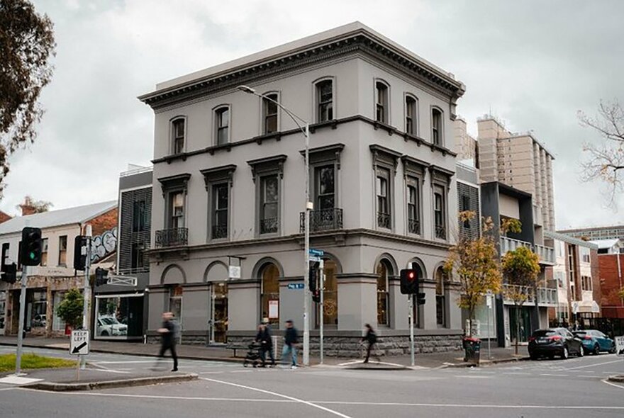 Three storey, white, Victorian-era building, on a corner, against cloudy sky backdrop. 