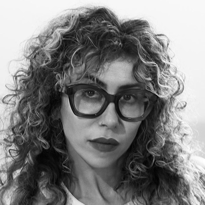Poet Ariana Reines, a woman with curly long hair, wearing heavy dark rimmed glasses.