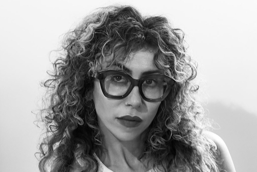 Poet Ariana Reines, a woman with curly long hair, wearing heavy dark rimmed glasses.