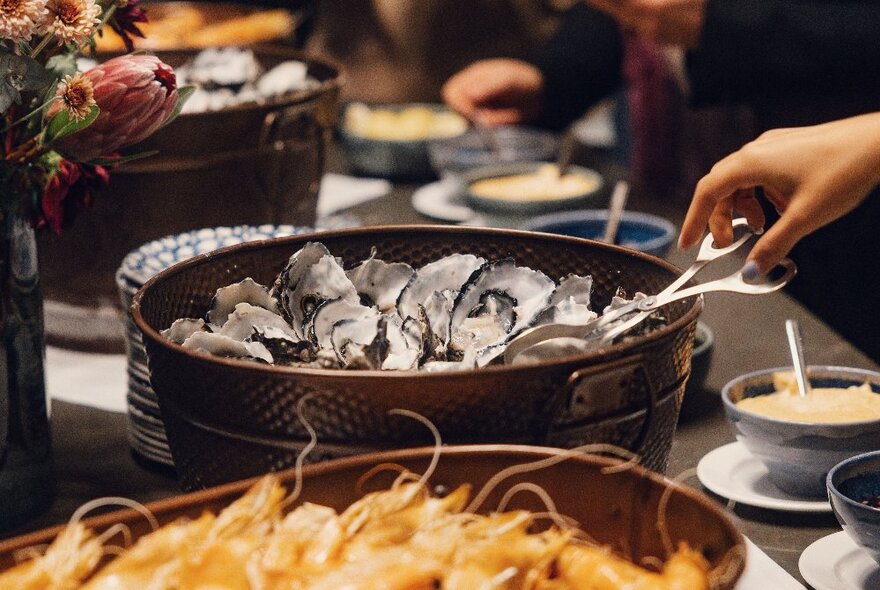 A hand on tongs selecting an oyster from a bucket at a buffet table. 