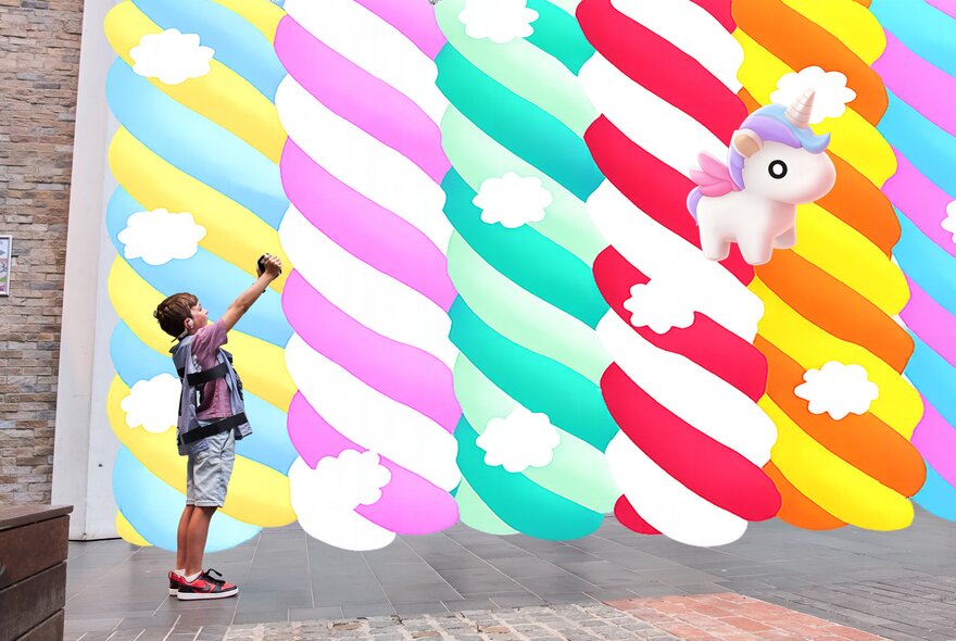 A child wearing a purple vest holding an Augmented Reality device up in front of a digital image of a rainbow and a unicorn.