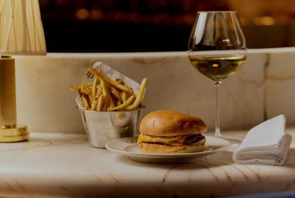 A cheeseburger, fries and white wine in a fine dining restaurant.