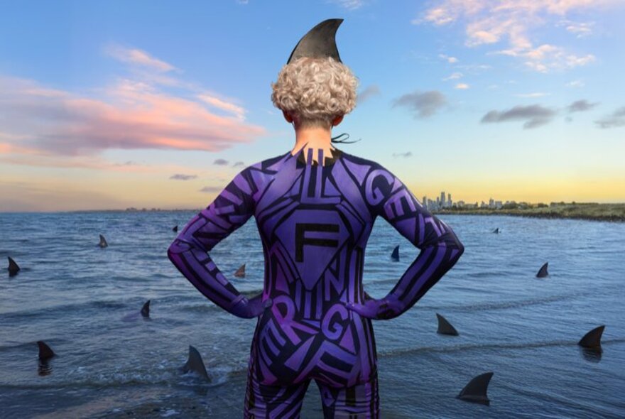 Person viewed from behind with hands on hips and shark fin on head, looking at bay filled with shark fins.