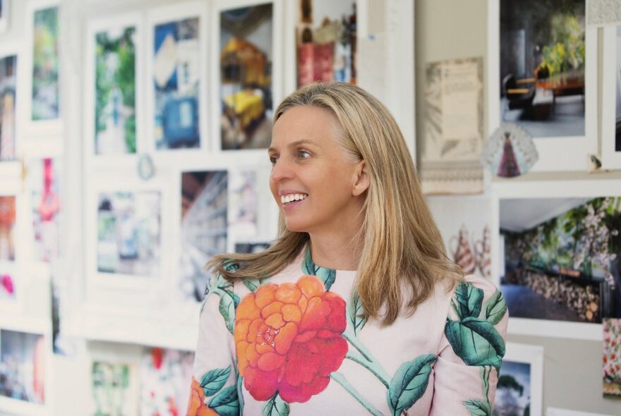 Photographer Robyn Lea standing in front of a wall display of images.