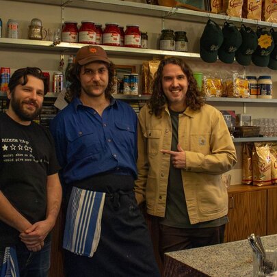 Three people smiling behind a bar and kitchen counter.
