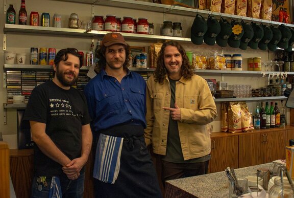 Three people smiling behind a bar and kitchen counter.